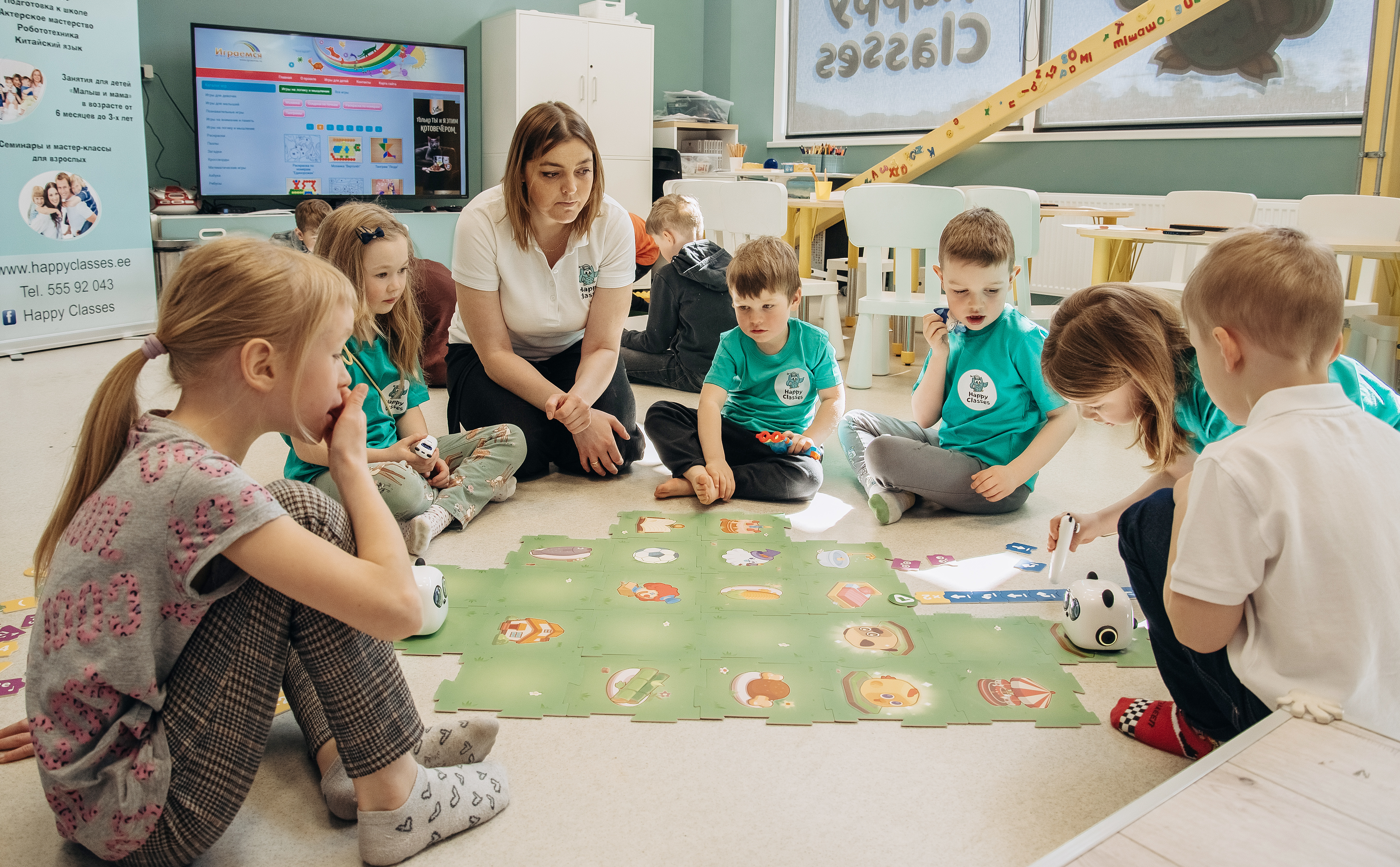 Õpetaja ja lapsed Happy Classesi tunnis põrandamängu ja robotitega